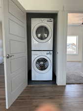 Laundry area with dark wood-style floors, a ceiling fan, stacked washer / dryer, laundry area, and baseboards