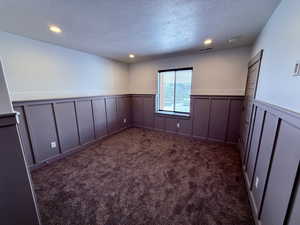 Spare room featuring a wainscoted wall, dark carpet, a textured ceiling, and recessed lighting