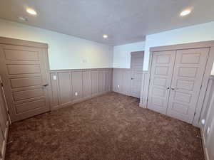 Unfurnished bedroom with a textured ceiling, recessed lighting, a wainscoted wall, carpet flooring, and a closet