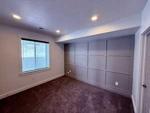 Empty room with dark colored carpet, recessed lighting, visible vents, a textured ceiling, and baseboards