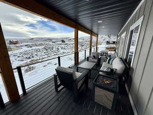 Snow covered deck featuring a mountain view and a fire pit