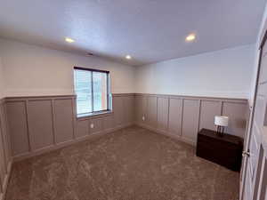 Empty room featuring light carpet, visible vents, a decorative wall, and a textured ceiling