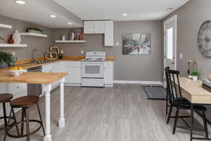 Kitchen featuring light hardwood / wood-style floors, white cabinetry, butcher block countertops, electric stove, and sink