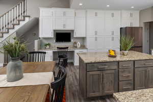 Kitchen with white cabinetry, light stone countertops, stainless steel refrigerator, and dark hardwood / wood-style flooring