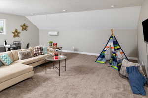 Living room with a wall mounted air conditioner, carpet, and lofted ceiling