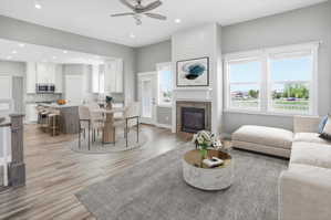 Open-concept living area with light-toned wood-finish flooring, a contemporary fireplace with wood-tile surround and shiplap accent, and a kitchen featuring white cabinetry and stainless steel appliances