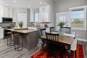 Kitchen featuring light hardwood / wood-style floors, white cabinets, a kitchen island, and appliances with stainless steel finishes