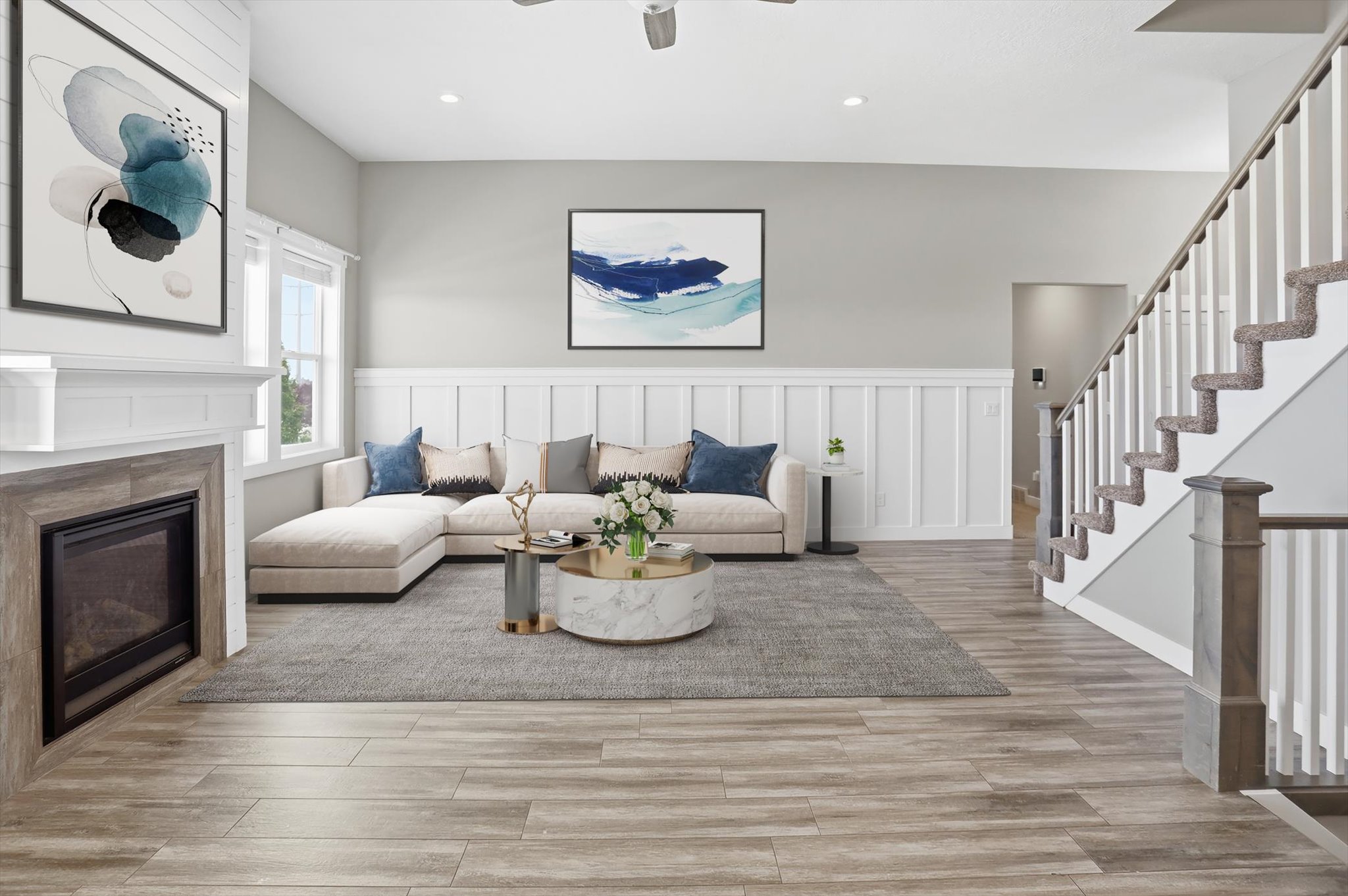 Spacious living area featuring wood-finish flooring, a fireplace with a wood-look surround, wainscoting details, and a carpeted staircase with white risers and balusters