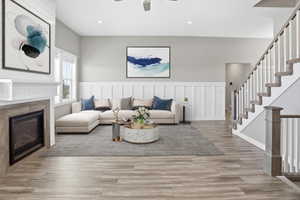 Spacious living area featuring wood-finish flooring, a fireplace with a wood-look surround, wainscoting details, and a carpeted staircase with white risers and balusters