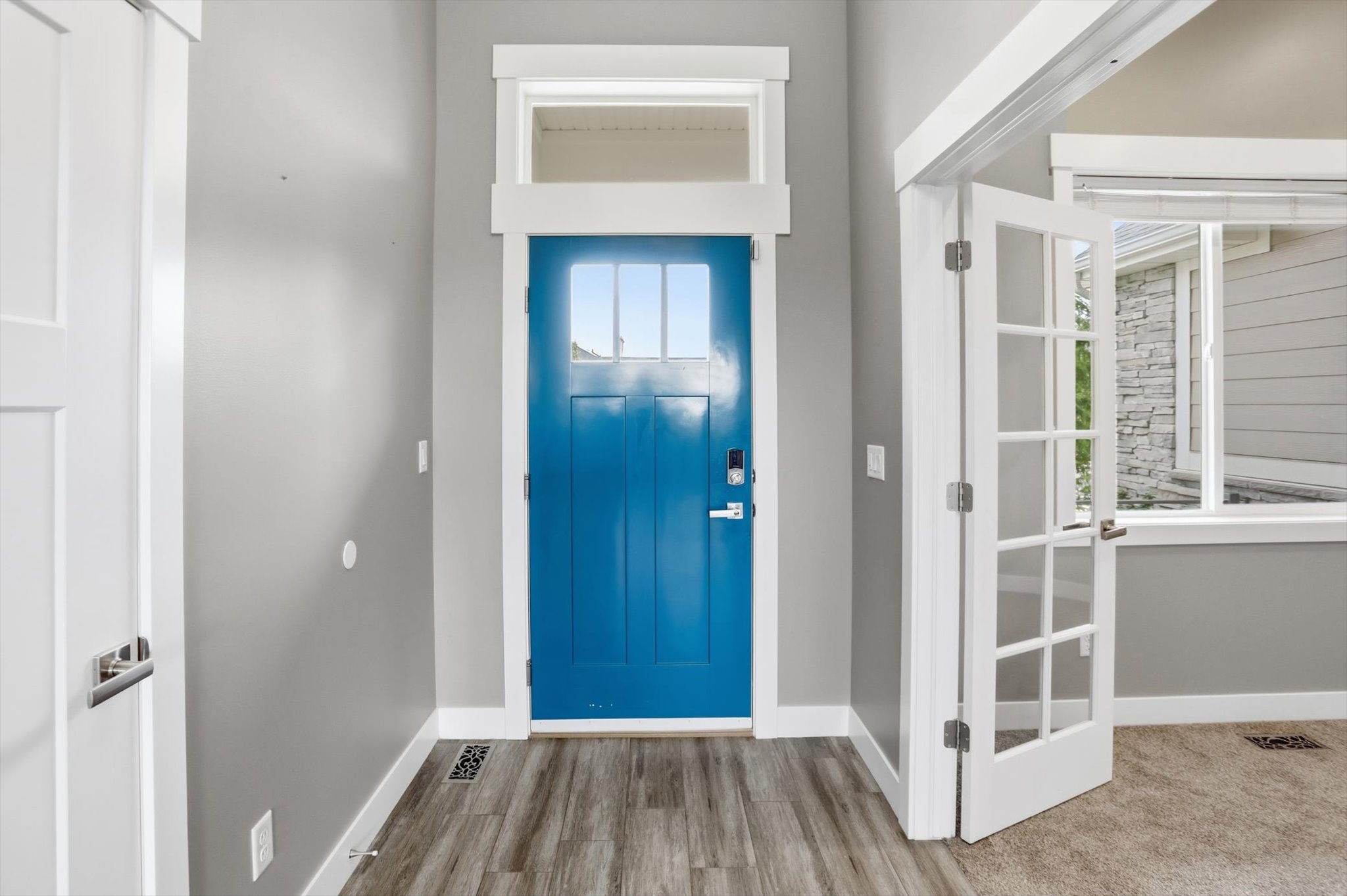 Entryway featuring a bright blue front door with upper glass panes, overhead transom window, and a smart lock system