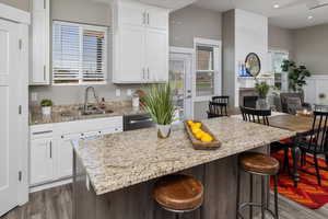 Kitchen featuring white cabinetry, a kitchen island, a breakfast bar area, light stone counters, and sink