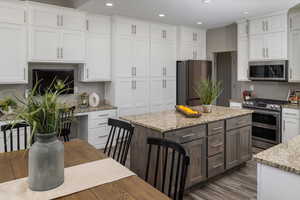 Kitchen featuring white cabinetry, a kitchen island, stainless steel appliances, hardwood / wood-style flooring, and light stone counters