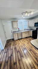 Kitchen with dark wood-type flooring, black range, sink, dishwasher, and light brown cabinets