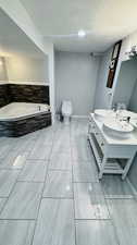 Bathroom with tile flooring, tiled tub, a textured ceiling, toilet, and vanity