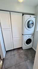 Clothes washing area with tile flooring, stacked washer / drying machine, and cabinets