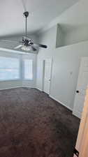 Unfurnished room featuring lofted ceiling, dark colored carpet, and ceiling fan