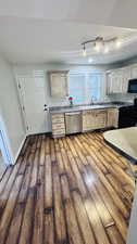 Kitchen with dark hardwood / wood-style flooring, black appliances, rail lighting, sink, and light brown cabinets