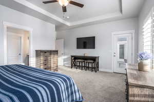 Bedroom with light carpet, ceiling fan, multiple windows, and a raised ceiling