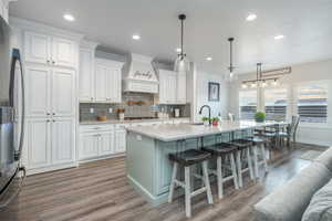 Kitchen with stainless steel appliances, white cabinets, hardwood / wood-style flooring, and premium range hood