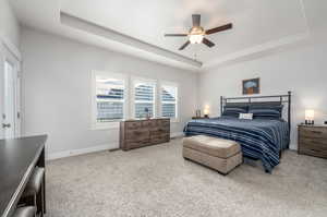 Carpeted bedroom featuring ceiling fan and a tray ceiling