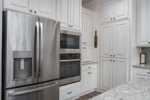 Kitchen with stainless steel appliances, dark wood-type flooring, light stone counters, and white cabinetry