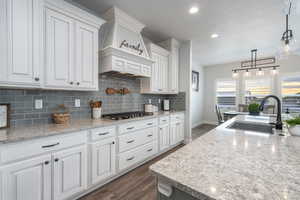 Kitchen with dark hardwood / wood-style floors, decorative light fixtures, white cabinetry, and backsplash