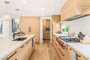 Kitchen featuring decorative light fixtures, custom range hood, light hardwood / wood-style floors, light brown cabinetry, and sink