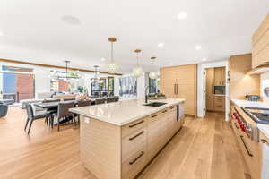 Kitchen with light brown cabinets, light hardwood / wood-style floors, a large island with sink, hanging light fixtures, and sink