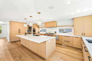 Kitchen featuring light hardwood / wood-style flooring, a kitchen island with sink, sink, light brown cabinetry, and custom exhaust hood