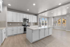 Kitchen featuring stainless steel appliances, light hardwood / wood-style floors, tasteful backsplash, and white cabinetry