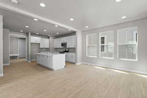 Kitchen featuring light hardwood / wood-style floors, stainless steel appliances, white cabinetry, an island with sink, and sink