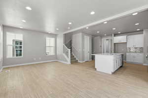 Kitchen featuring light hardwood / wood-style floors, white cabinetry, an island with sink, backsplash, and sink