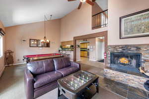 Tiled living room with a stone fireplace, ceiling fan with notable chandelier, pool table, and high vaulted ceiling