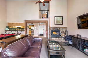 Living room with a stone fireplace, a high ceiling, ceiling fan, and pool table