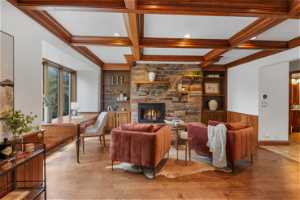 Living room featuring coffered ceiling, built in features, a stone fireplace, beam ceiling, and hardwood floors