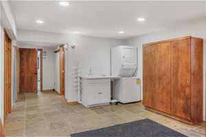 Laundry area featuring stacked washer and clothes dryer, sink, and light tile flooring