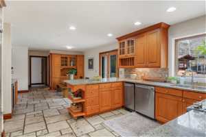 Kitchen with light stone counters, tasteful backsplash, stainless steel dishwasher, sink, and light tile floors
