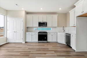 Kitchen featuring white cabinetry, light wood-type flooring, stainless steel appliances, backsplash, and sink