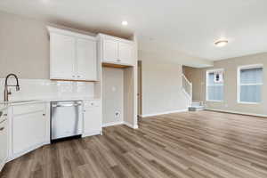 Kitchen featuring light hardwood / wood-style floors, tasteful backsplash, dishwasher, sink, and white cabinets