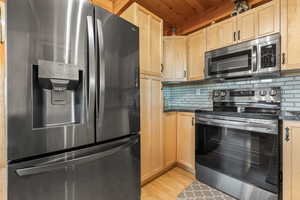 Kitchen with tasteful backsplash, light wood-type flooring, wood ceiling, and appliances with stainless steel finishes