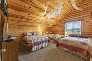 Carpeted bedroom featuring vaulted ceiling, rustic walls, ceiling fan, and wood ceiling