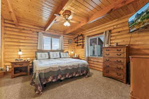 Carpeted bedroom featuring wooden ceiling, ceiling fan, rustic walls, and beam ceiling