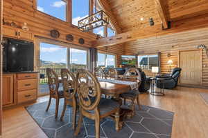 Dining room featuring light hardwood / wood-style flooring, beam ceiling, wood ceiling, rustic walls, and high vaulted ceiling