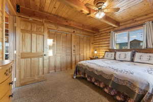 Carpeted bedroom with ceiling fan, wooden ceiling, two closets, beamed ceiling, and rustic walls