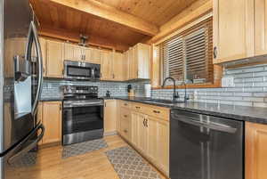 Kitchen with light hardwood / wood-style floors, backsplash, beam ceiling, appliances with stainless steel finishes, and sink