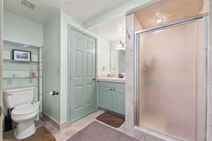 Bathroom with tile floors, a shower with shower door, vanity, and toilet