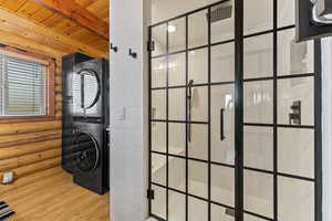 Clothes washing area featuring stacked washer / drying machine, light hardwood / wood-style flooring, rustic walls, and wooden ceiling