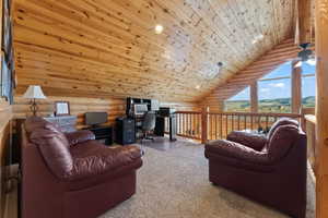 Carpeted living room with high vaulted ceiling, wooden ceiling, rustic walls, and ceiling fan