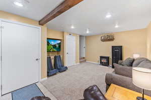 Living room with beam ceiling, carpet floors, and a wood stove