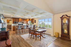 Dining space with beam ceiling, light hardwood / wood-style floors, coffered ceiling, and decorative columns